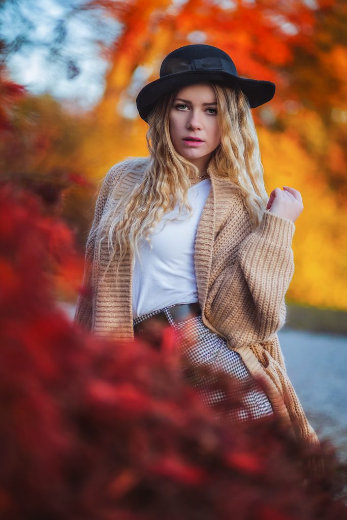 Herbst-Fotoshooting Portrait mit Model im Casual Look, trägt Wolljacke, sitzt zwischen bunten Herbstblättern im Wald – goldenes Licht, natürliche Herbstfarben und warme Autumn Colors