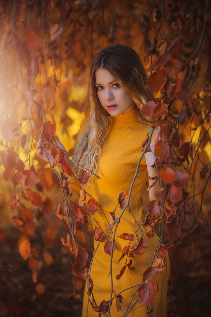 Herbst Fotoshooting mit Model in klassischem orangem Outfit, verführerisch und natürlich, posierend im herbstlichen Wald bei goldenem Licht – warme Autumn Colors und dezente Fantasy Fotoshooting-Stimmung. Aufnahme von Elena Frizler Photography in Luzern, Schweiz