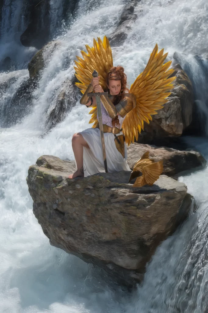 Elena-Frizler-fotografiert-epische-Walküre-in-goldener-Rüstung,-sitzend-und-stehend-auf-Felsen,-umgeben-von-gigantischem-Wasserfall