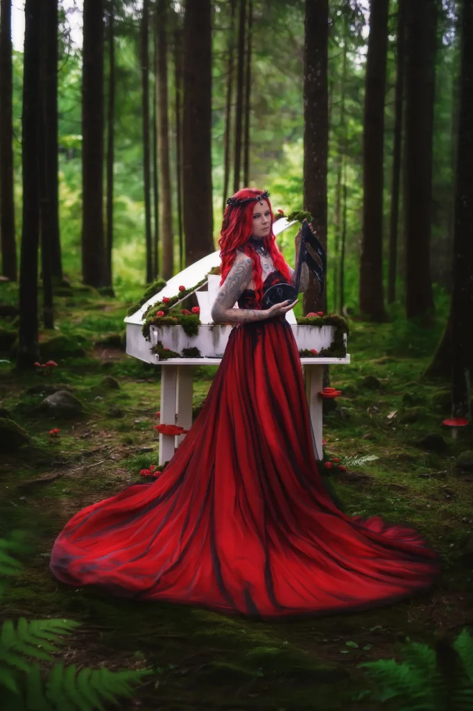 Frau-mit-roten-Haaren-im-roten-Kleid-steht-verträumt-im-Wald-neben-einem-verwunschenen-weißen-Piano-–-Elena-Frizler-Photography