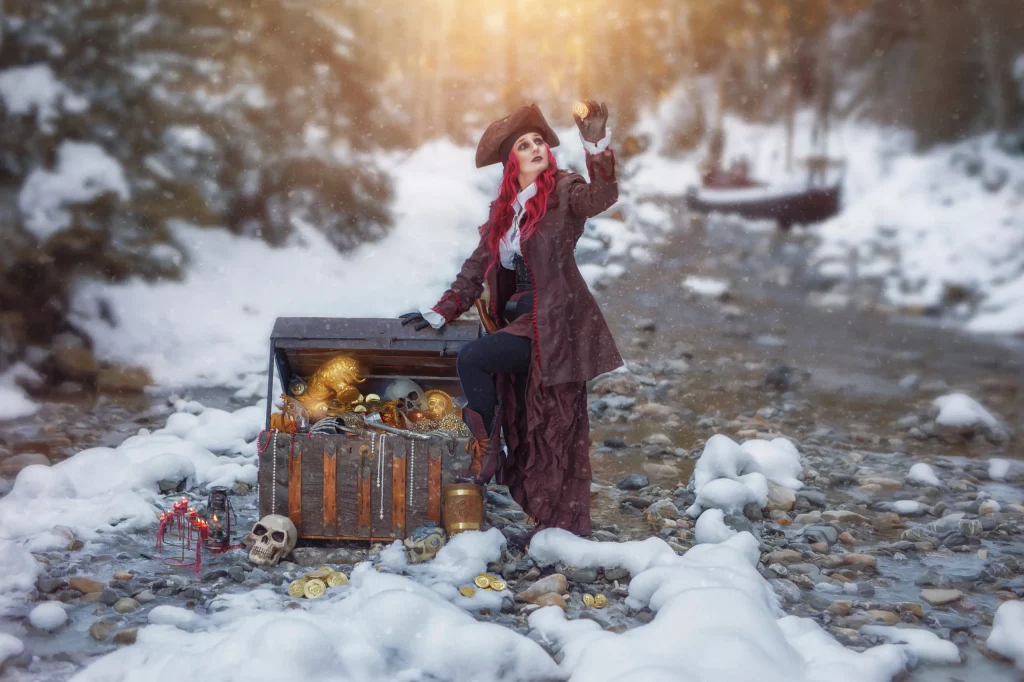 Piratenfrau-im-Cosplay-neben-Schatztruhe-voller-Gold-in-vereistem-Waldbach-im-verschneiten-Wald-–-Elena-Frizler-Photography