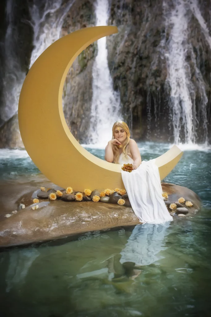 Kniendes Model hinter riesigem Sichelmond, umgeben von gelben Blüten, magischer Wasserfall im Hintergrund – Fantasy-Fotoshooting von Elena Frizler Photography, LuzernEntlebuch Schweiz.