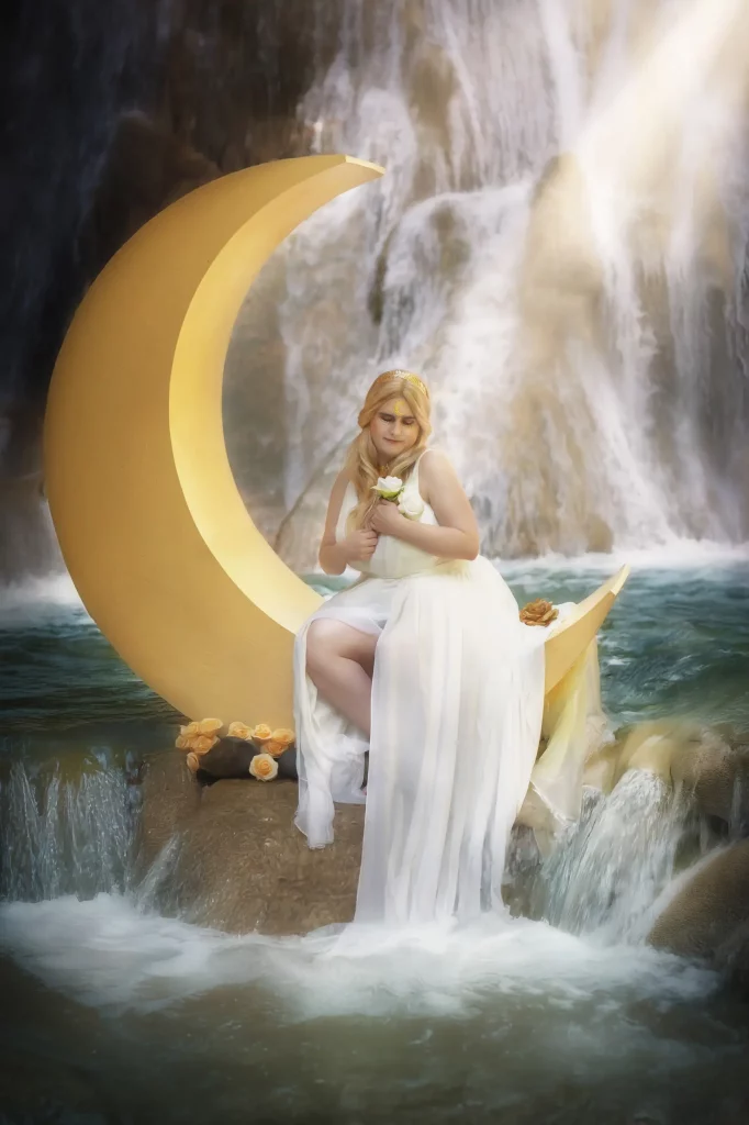 Model sitzend auf Sichelmond, hält Blume, wunderschönes Licht fällt von oben, Wasserfall im Hintergrund – Fantasy-Fotoshooting von Elena Frizler Photography, LuzernEntlebuch Schweiz.