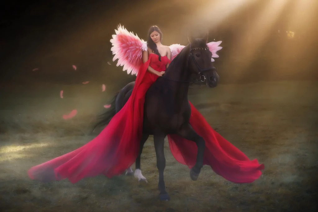 Fantasy Fotoshooting mit Pferd – Frau in rotem Kleid mit Engelsflügeln reitet im Sonnenlicht, Szene fotografiert von Elena Frizler Photography in der Schweiz.