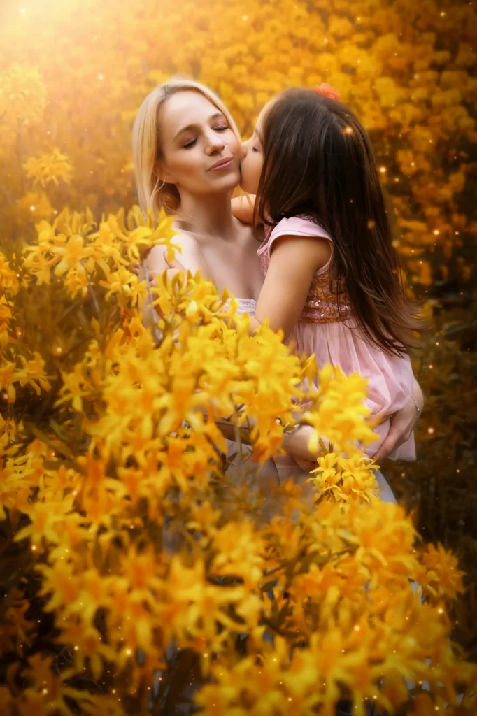 Mutter Tochter Fotoshooting in goldenem Blumenfeld mit liebevoller Umarmung warme emotionale Fine Art Fotografie Schweiz
