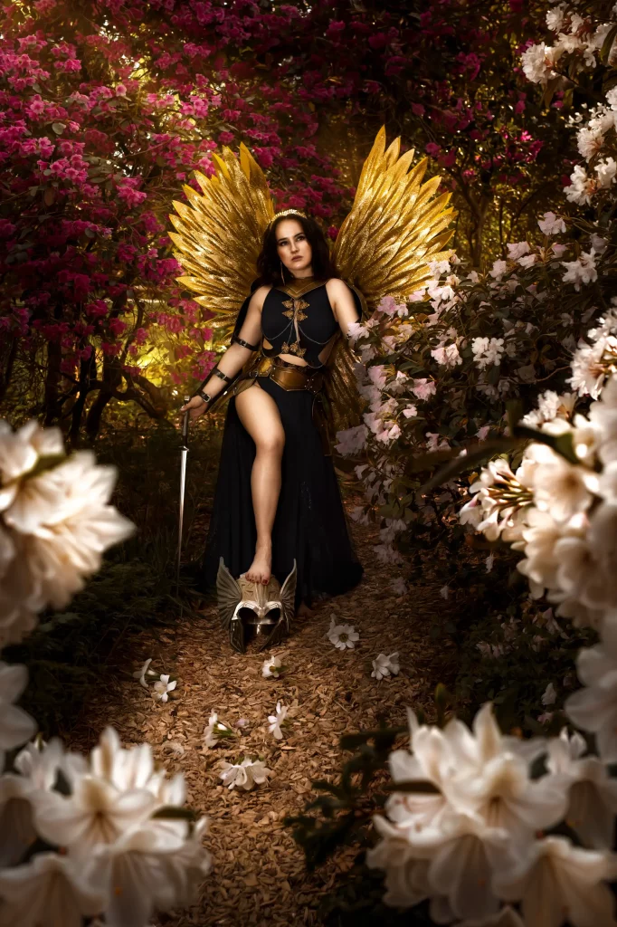 Cinematic Fine Art Portrait einer Walküre mit goldenen Flügeln zwischen rosa und weissen Blüten