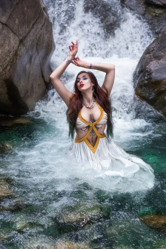Cinematic Fine Art Portrait einer Frau im türkisblauen Bergfluss vor einem Wasserfall