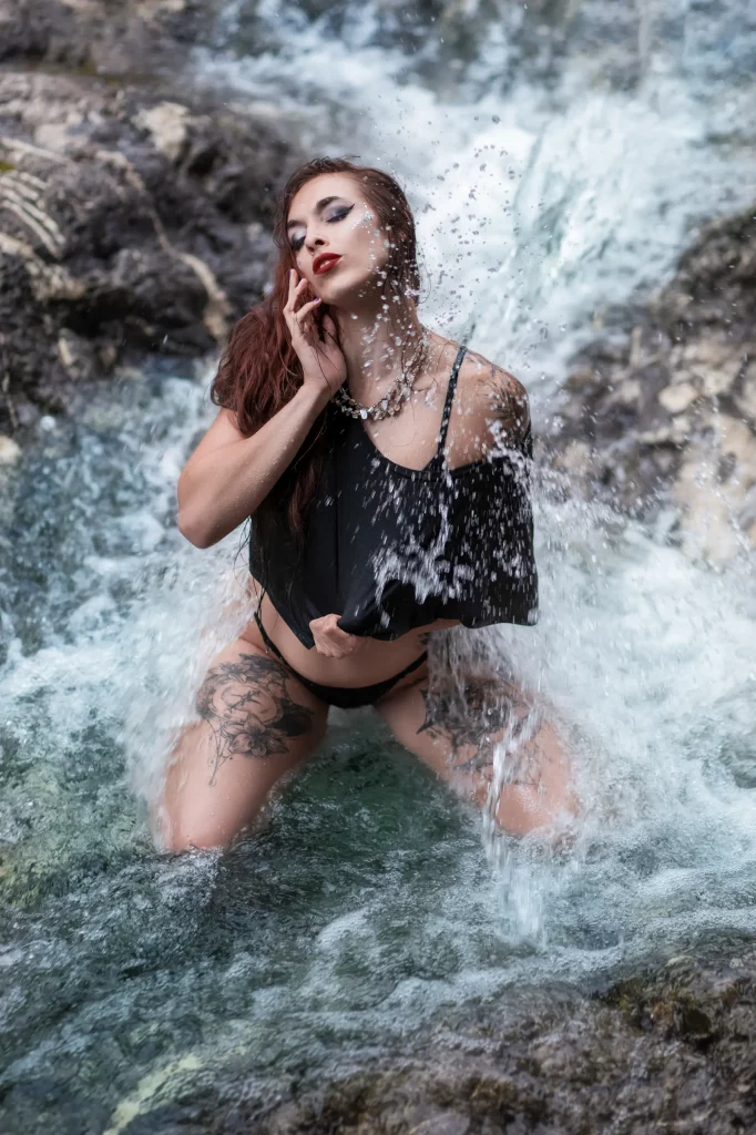 Cinematic Fine Art Portrait einer Frau unter einem Wasserfall im Bergfluss der Schweiz