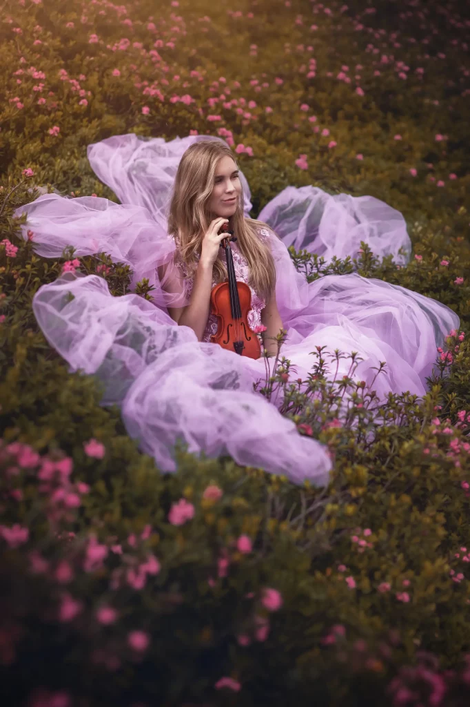 Frau mit Violine in einem rosa Bluetenfeld waehrend eines Fine Art Fotoshootings in den Schweizer Alpen