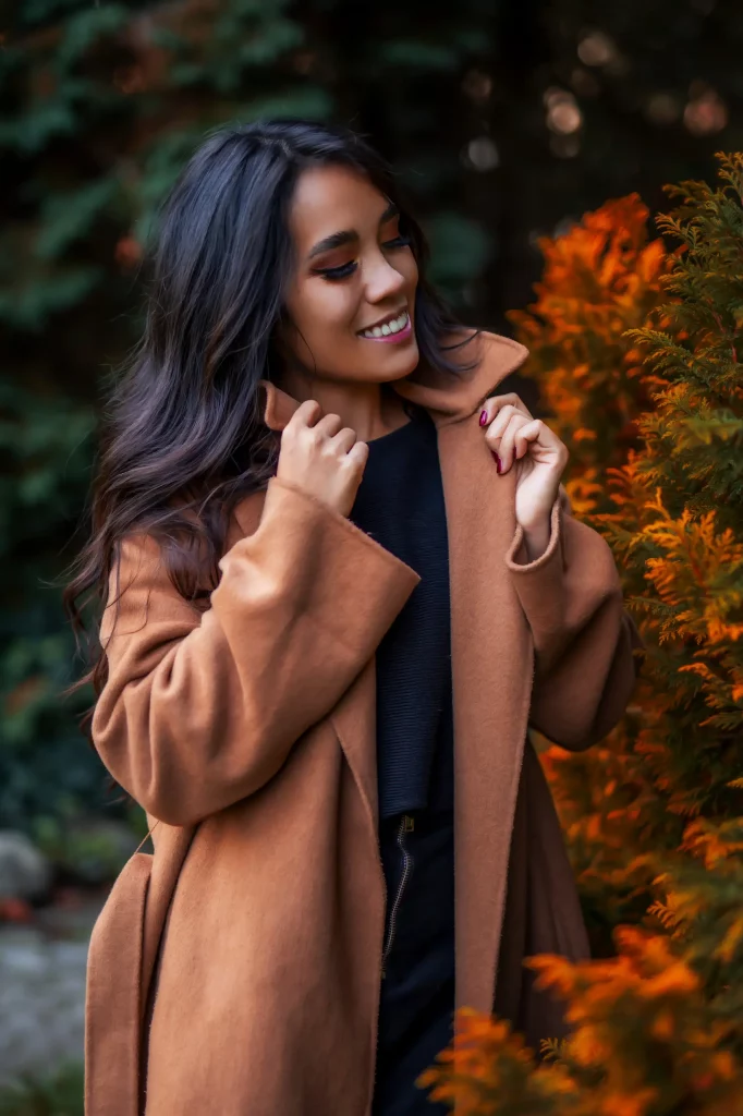 Herbstliches Portrait-Fotoshooting im Casual Look mit braunem Mantel zwischen leuchtenden Herbstfarben und immergrünen Pflanzen