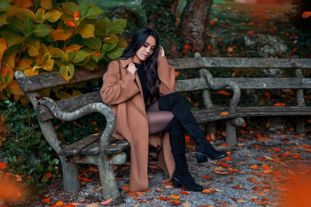 Herbstliches Portrait-Fotoshooting im Casual Look mit braunem Mantel auf einer rustikalen Bank zwischen buntem Herbstlaub
